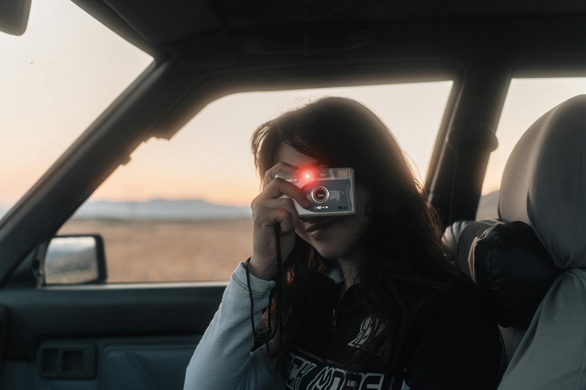 Kobieta siedząca w samochodzie fotografuje zachód słońca aparatem