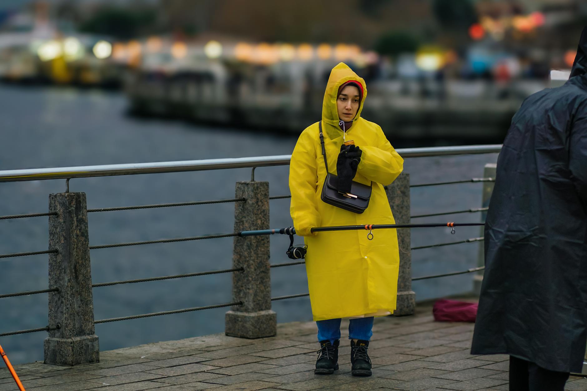 Kobieta w żółtym płaszczu przeciwdeszczowym nad wodą w pochmurny dzień