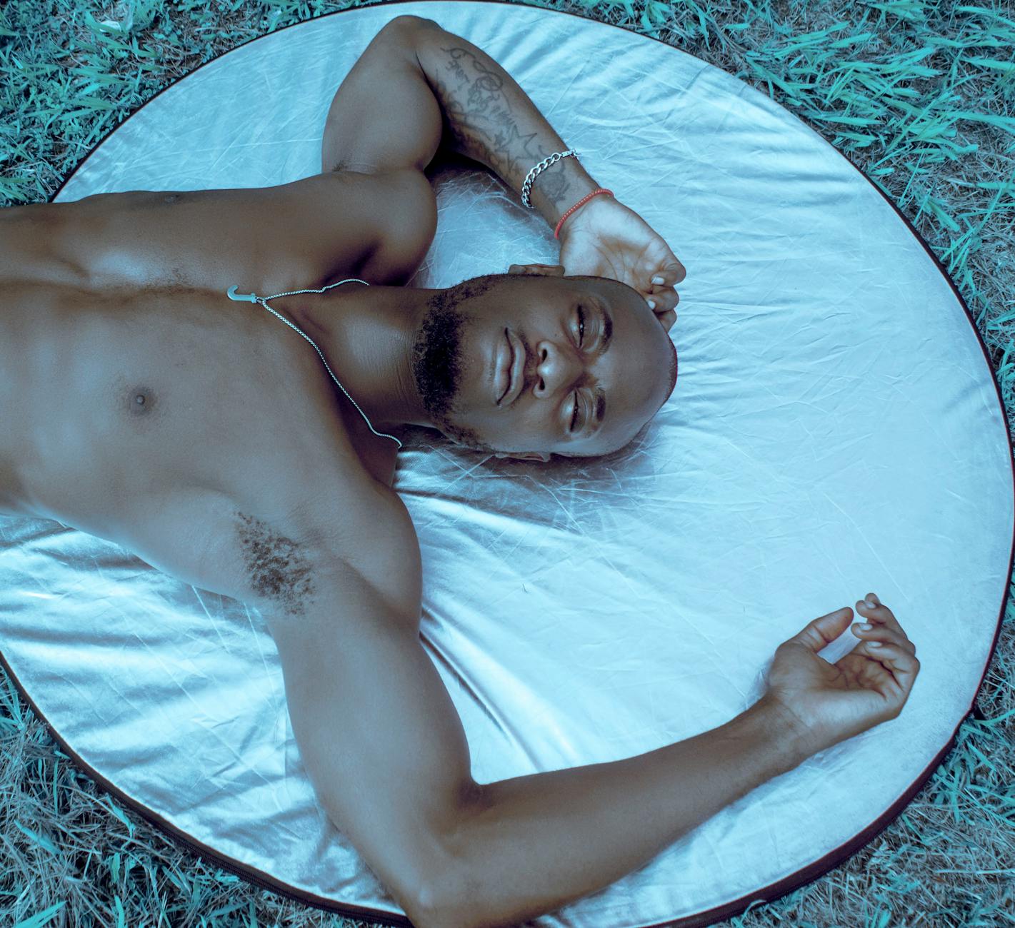 Mężczyzna z zamkniętymi oczami leży bez koszulki na refleksyjnym podłożu