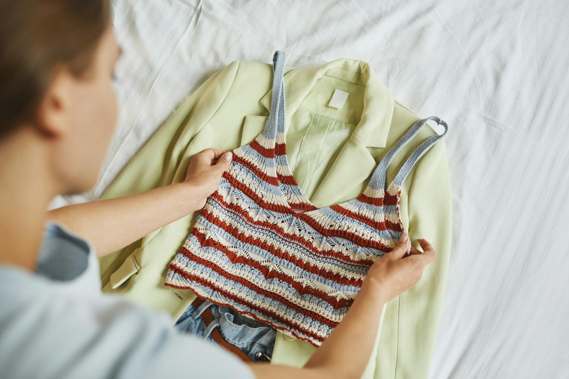 Kobieta układa na łóżku stylową marynarkę i dzianinowy top