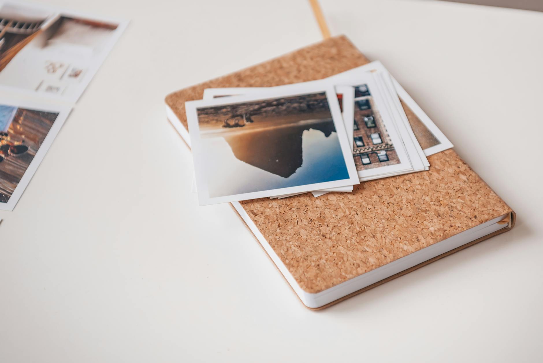 Notes z korkową okładką i wydrukowane zdjęcia podróżnicze na białym biurku