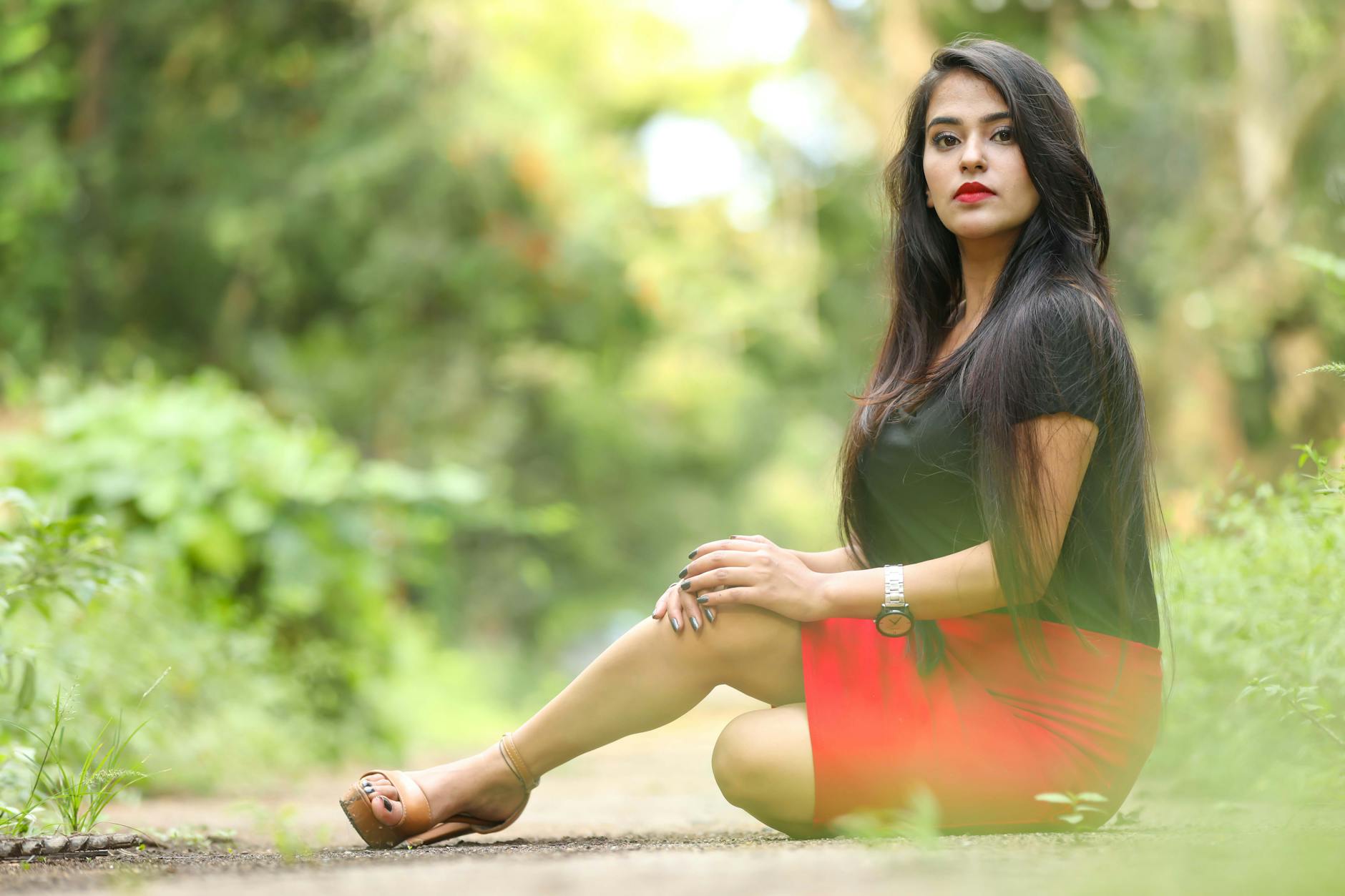 Elegancka Induska pozuje w zielonym plenerze, siedząc na murku