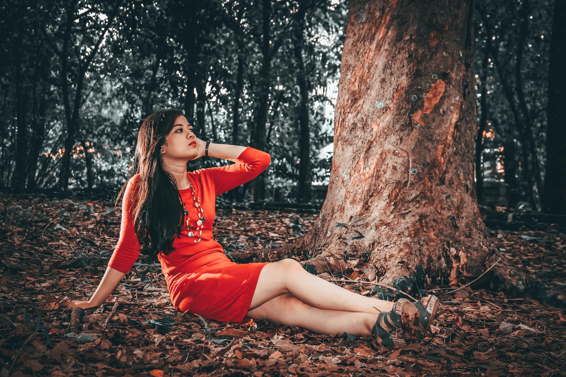 Kobieta w czerwonej sukni oparta o drzewo w spokojnym lesie