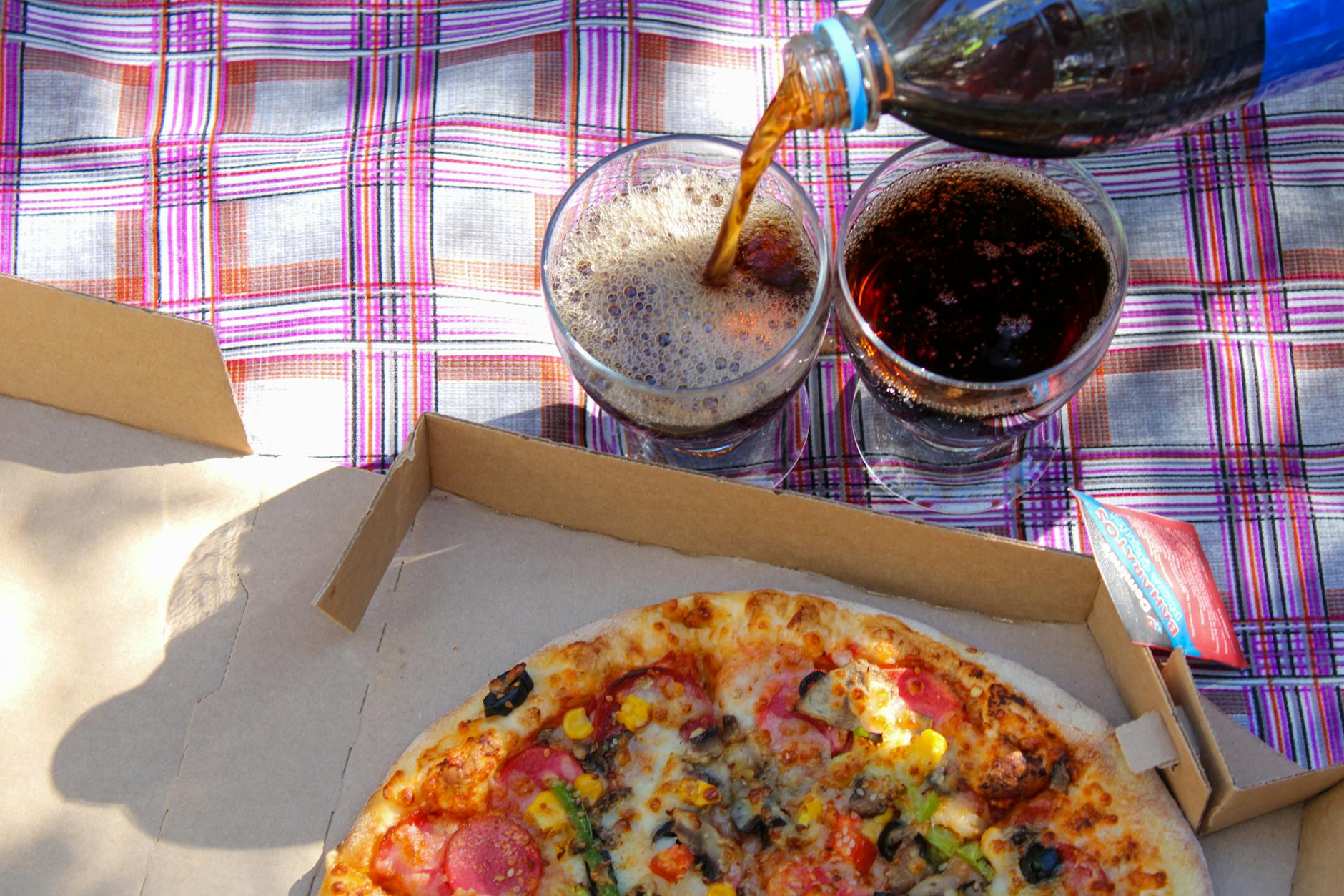 Pokrojona pizza i cola na kraciastym kocu piknikowym w parku