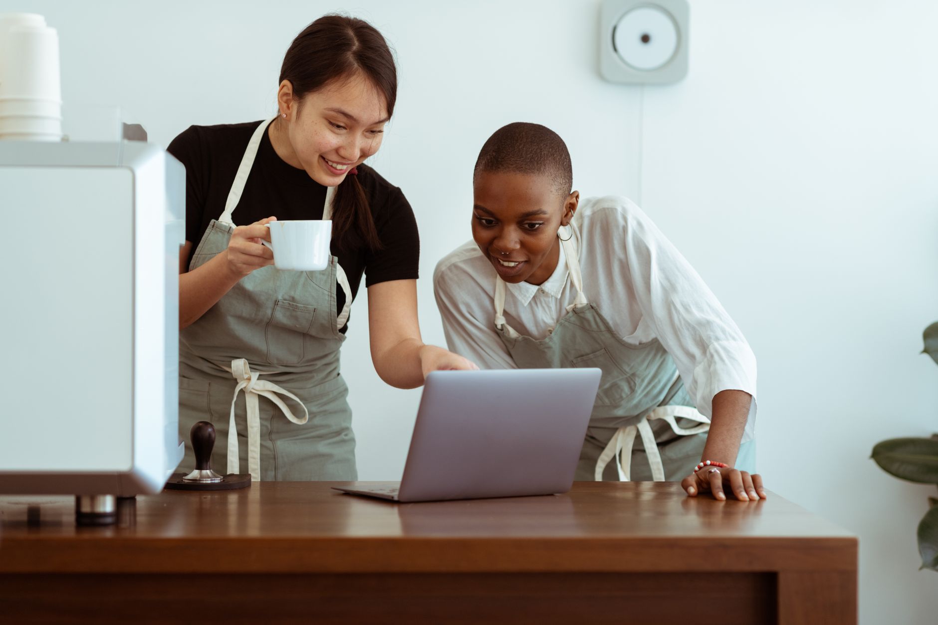 Kelnerki w fartuchach oglądają laptop w jasnej restauracyjnej kuchni