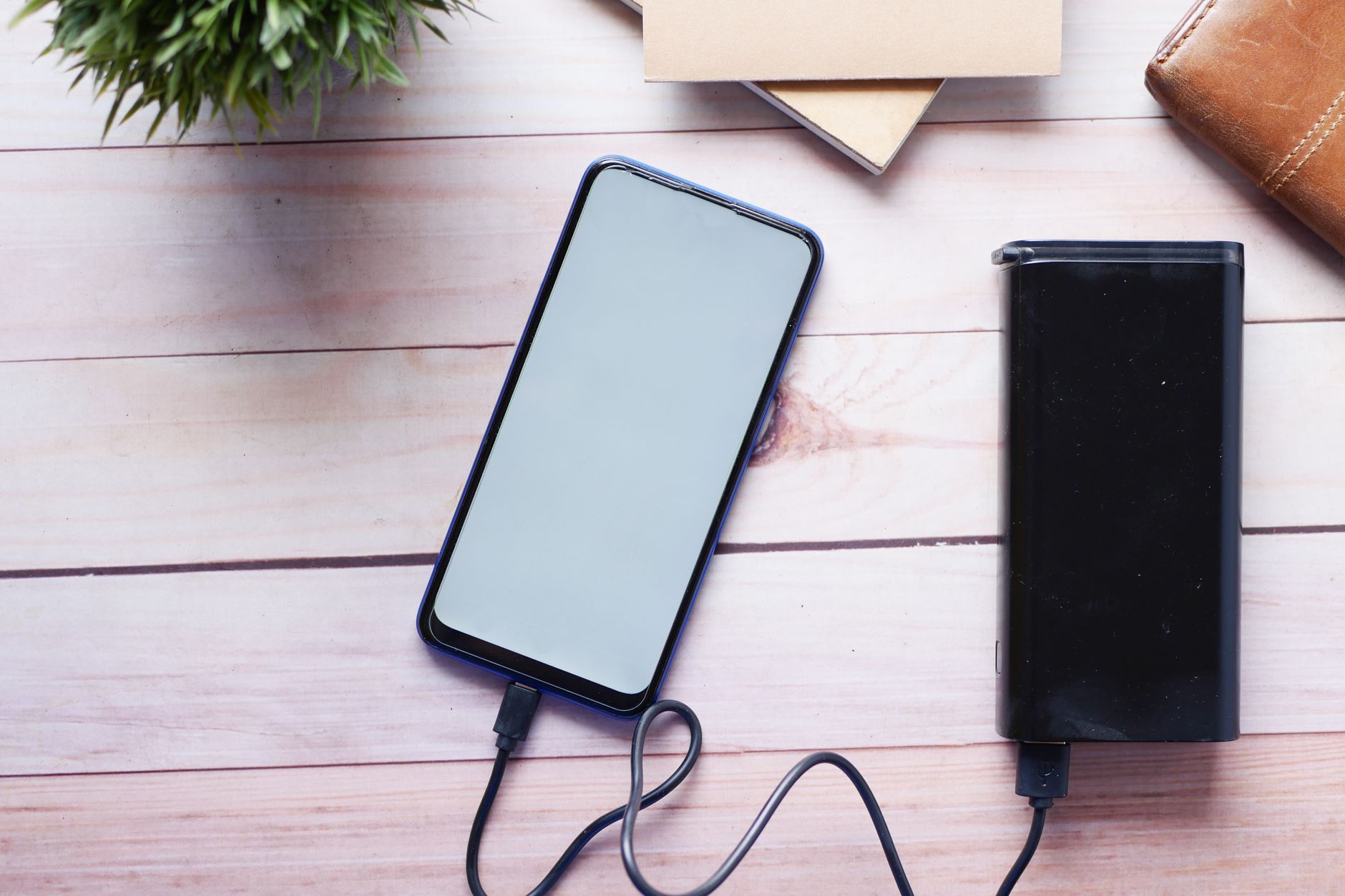 Smartfon ładowany z powerbanku leżący na drewnianym biurku